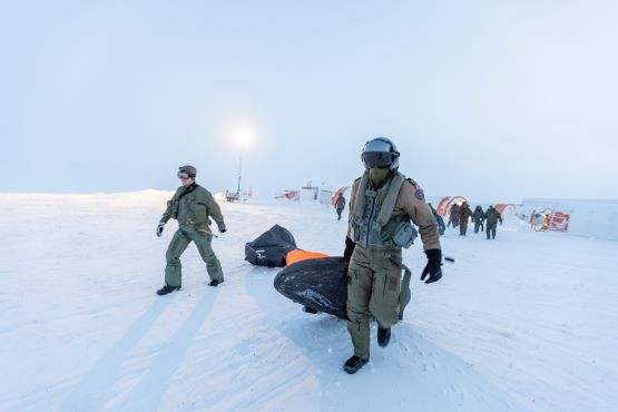 Un pilote des Forces armées canadiennes (à droite) et un pilote norvégien (à gauche) traînent une trousse de survie sur une plaine arctique.