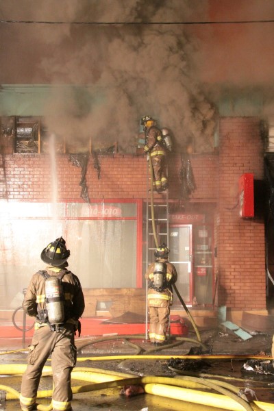 Les pompiers éteignent un feu dans un édifice de brique avec beaucoup de fumée foncée.