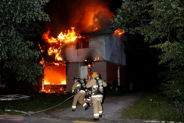 Deux pompiers courent pour éteindre un feu dans une maison.