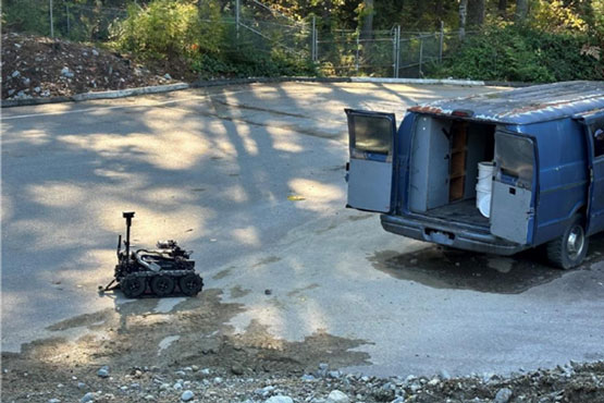 Un robot est sur le sol, à proximité d’une camionnette dont les portes sont ouvertes.