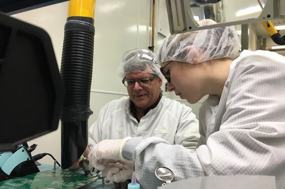 Deux personnes revêtant des sarraus et des filets à cheveux travaillent dans un laboratoire.