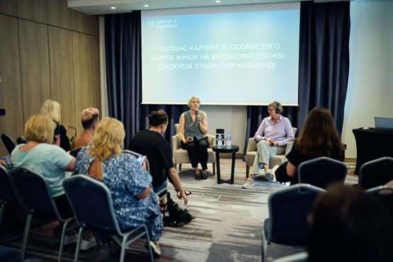 Deux personnes assises sur des chaises à l’avant d’une pièce s’adressent à un public.