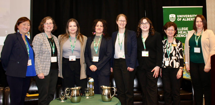 La photo montre huit femmes qui participaient à l’événement comme panélistes et conférencières ensemble devant un mur noir et une bannière de l’Université de l’Alberta.