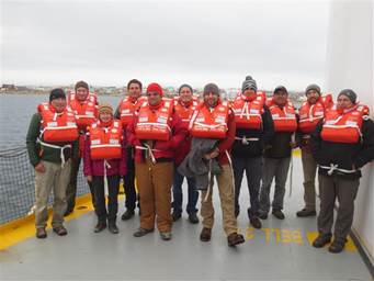 Membres d’équipage, après l’exercice de sécurité-incendie, sur le pont du navire Sir Wilfrid Laurier, avec Cambridge Bay en arrière-plan.