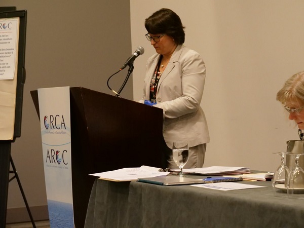 Un conférencier près d’une estrade devant laquelle se trouve le logo bilingue de l’AROC. 