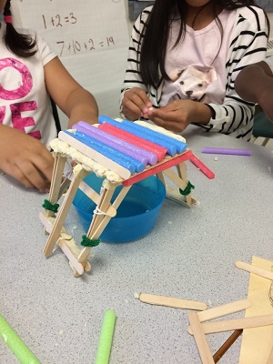 Two students prepare to test how much weight their bridge can hold before collapsing.