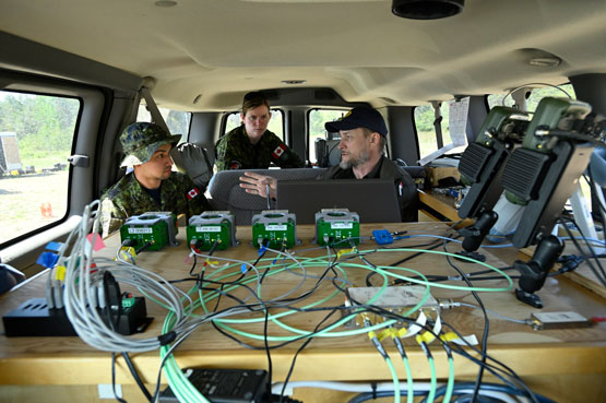 Trois personnes sont assises devant quatre récepteurs GPS verts reliés à de nombreux fils.