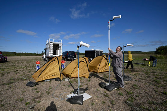 Une personne installe des antennes blanches à l’extérieur près de trois tentes jaunes.