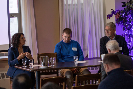 Trois personnes sont assises derrière une table lors d’une conférence.