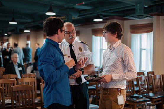 Une personne vêtue d’un uniforme du Service des incendies d’Ottawa discute de prototypes technologiques avec deux chercheurs.