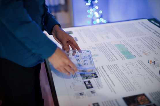 Une personne tient une boîte transparente avec des échantillons de capteur au-dessus d’une table affichant des renseignements techniques.