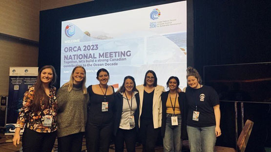 Un groupe de sept personnes associées à ECOP Canada devant une diapositive de présentation pour la réunion nationale de l’AROC 2023.