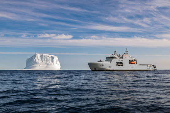 Un navire gris de la Marine royale canadienne, le NCSM Harry DeWolf, est photographié à côté d’un iceberg.